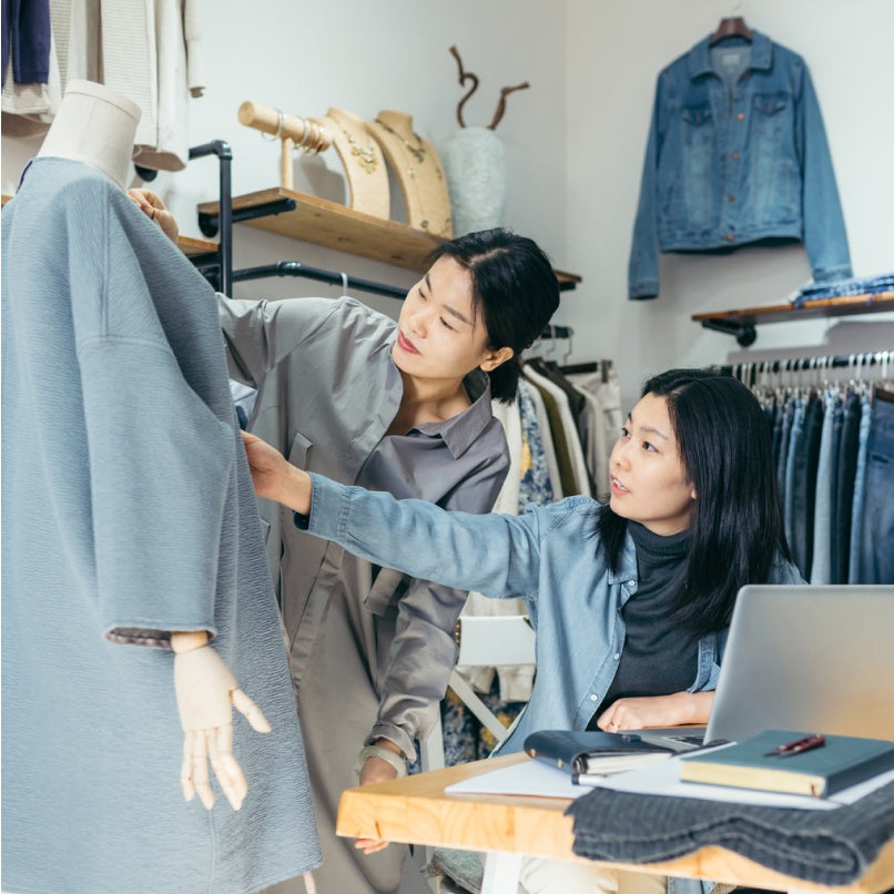 Two women in a store touching a jacket on mannequin, with denim jeans and jackets in background.