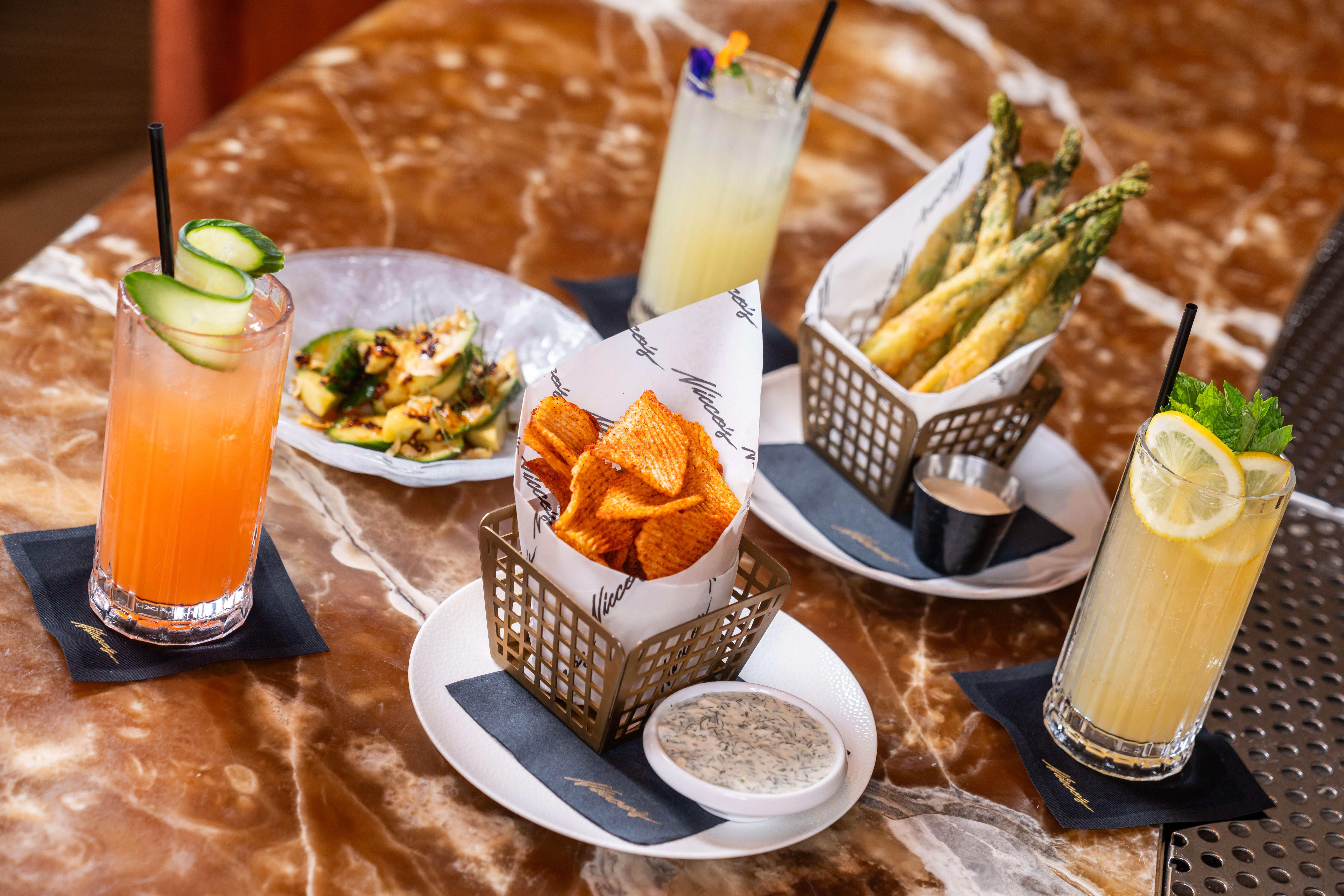 A marble table with cocktails, tempura asparagus, and a basket of fries. 