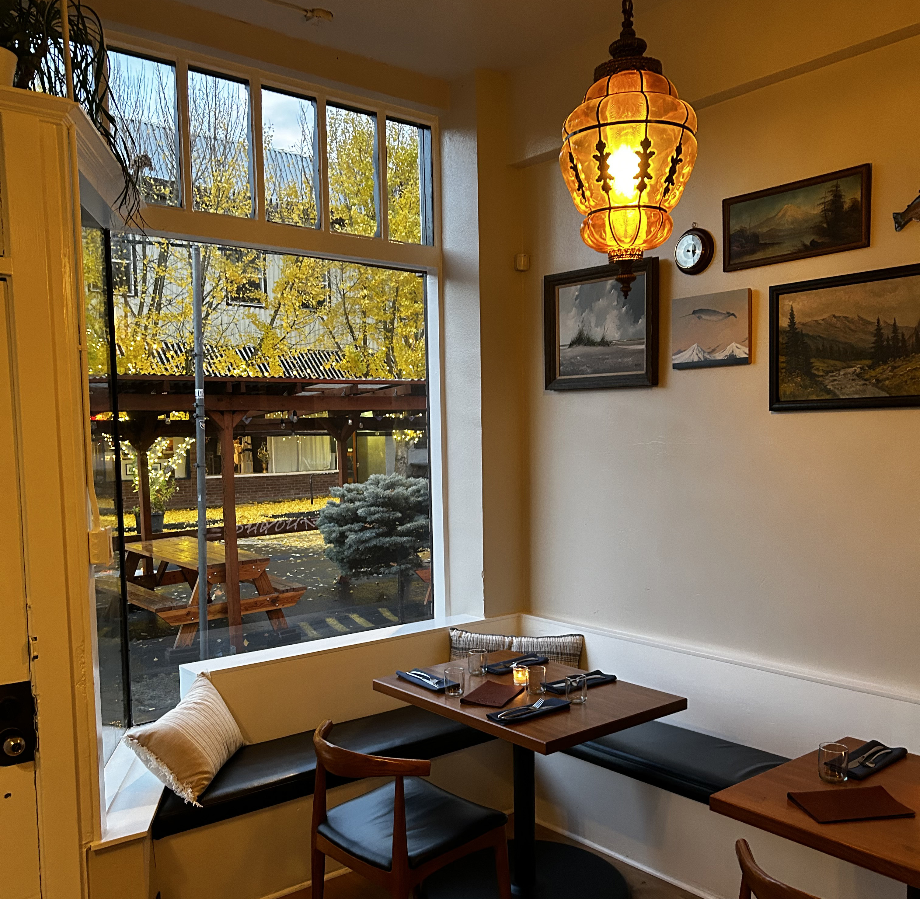 The warmly lit front nook of a restaurant with tables looking out into the street.