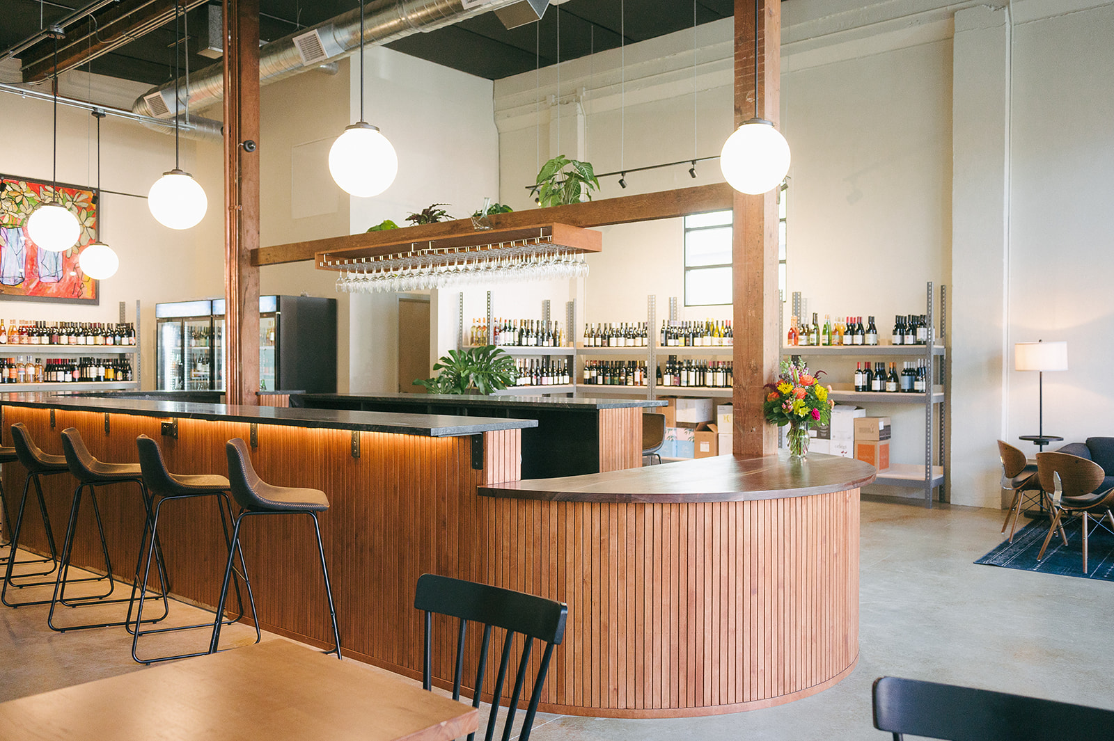 The interior of a wine bar with a wood-slatted, marble topped, oval-shaped bar at the center.