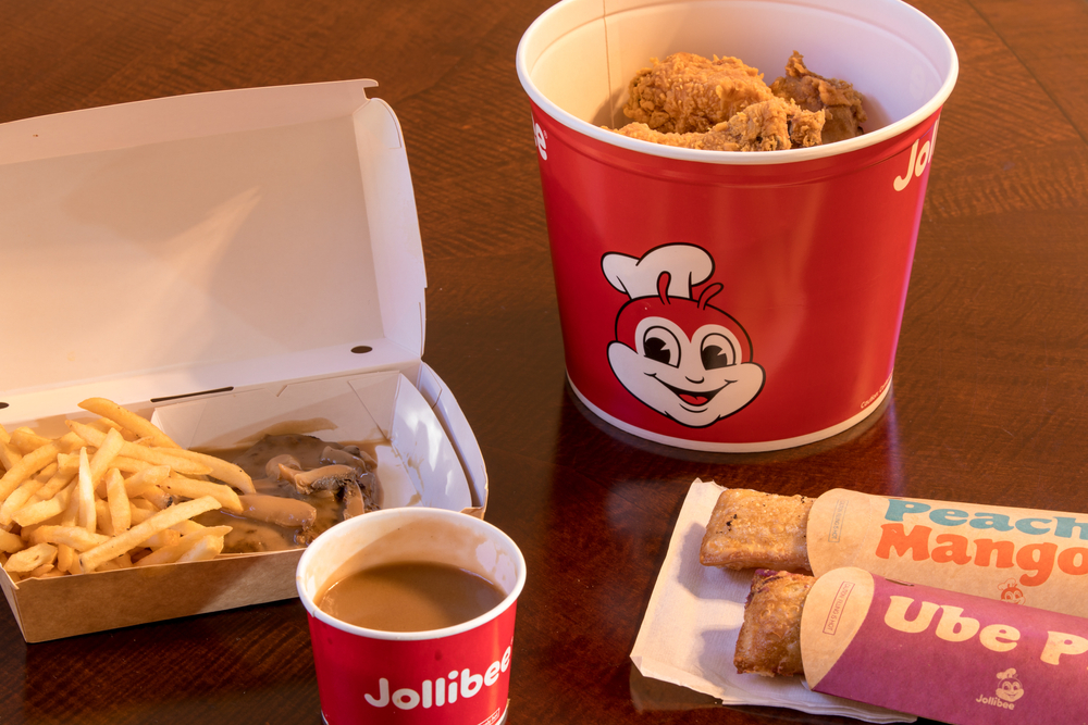 A box of fries and burger steak, a cup of gravy, a bucket of fried chicken, and hand pies from Jollibee.