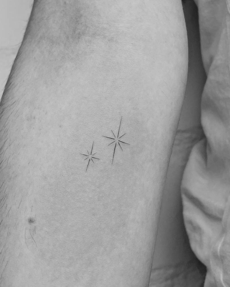 Fine line little stars tattooed on the inner forearm, minimalistic style.