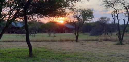 a sunset in a field with trees and a house at Grootgeluk in Naboomspruit