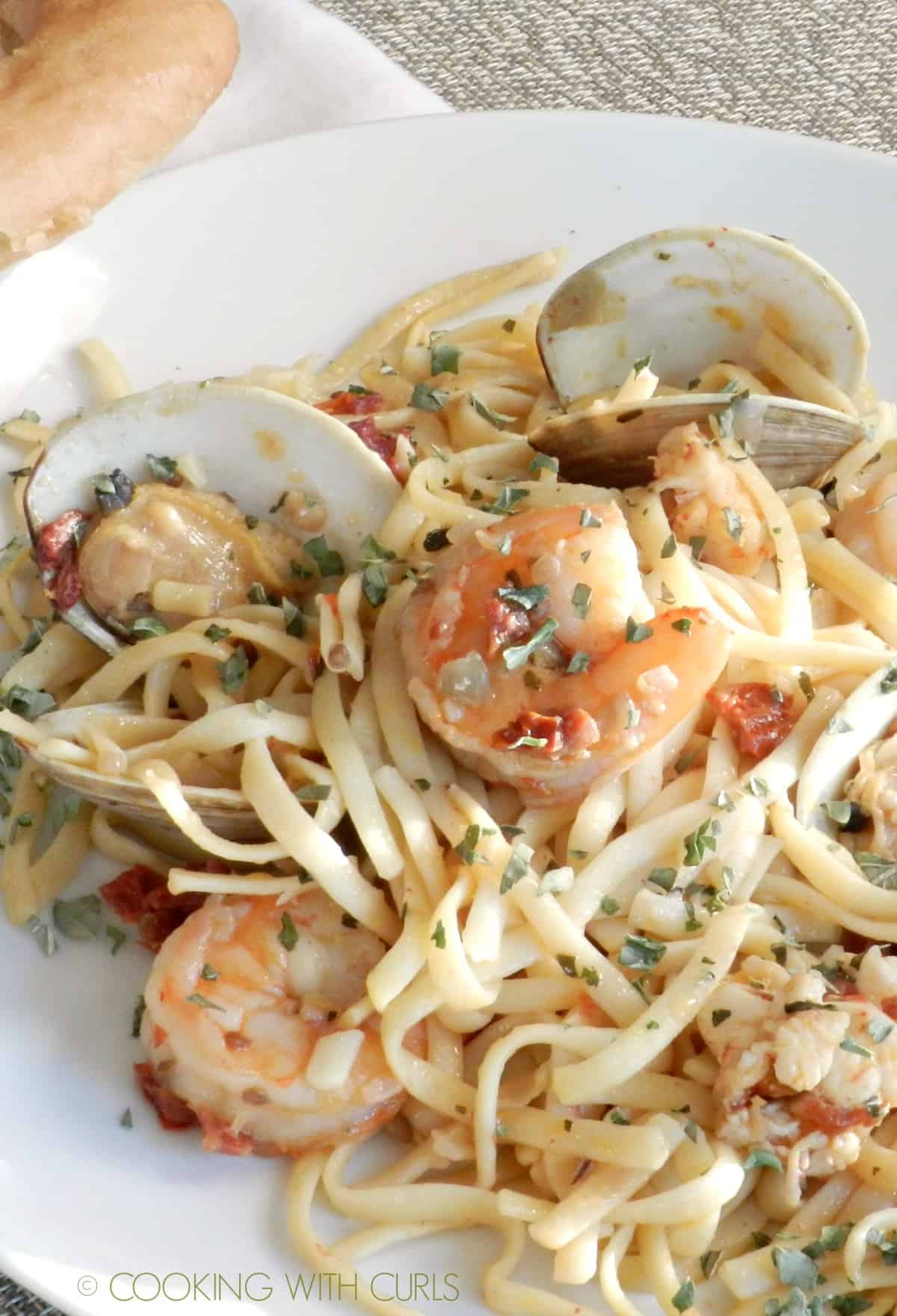 A large white plate with shrimp, clams and noodles in a garlic sauce.