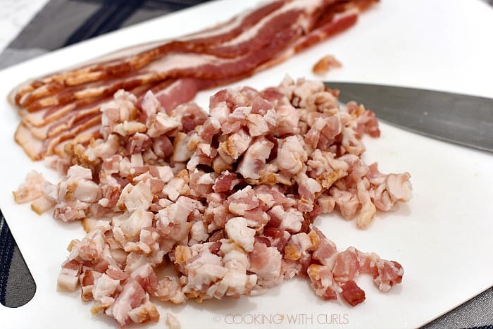 Bacon slices and chopped bacon on a white cutting board with a chef knife on the right hand side.