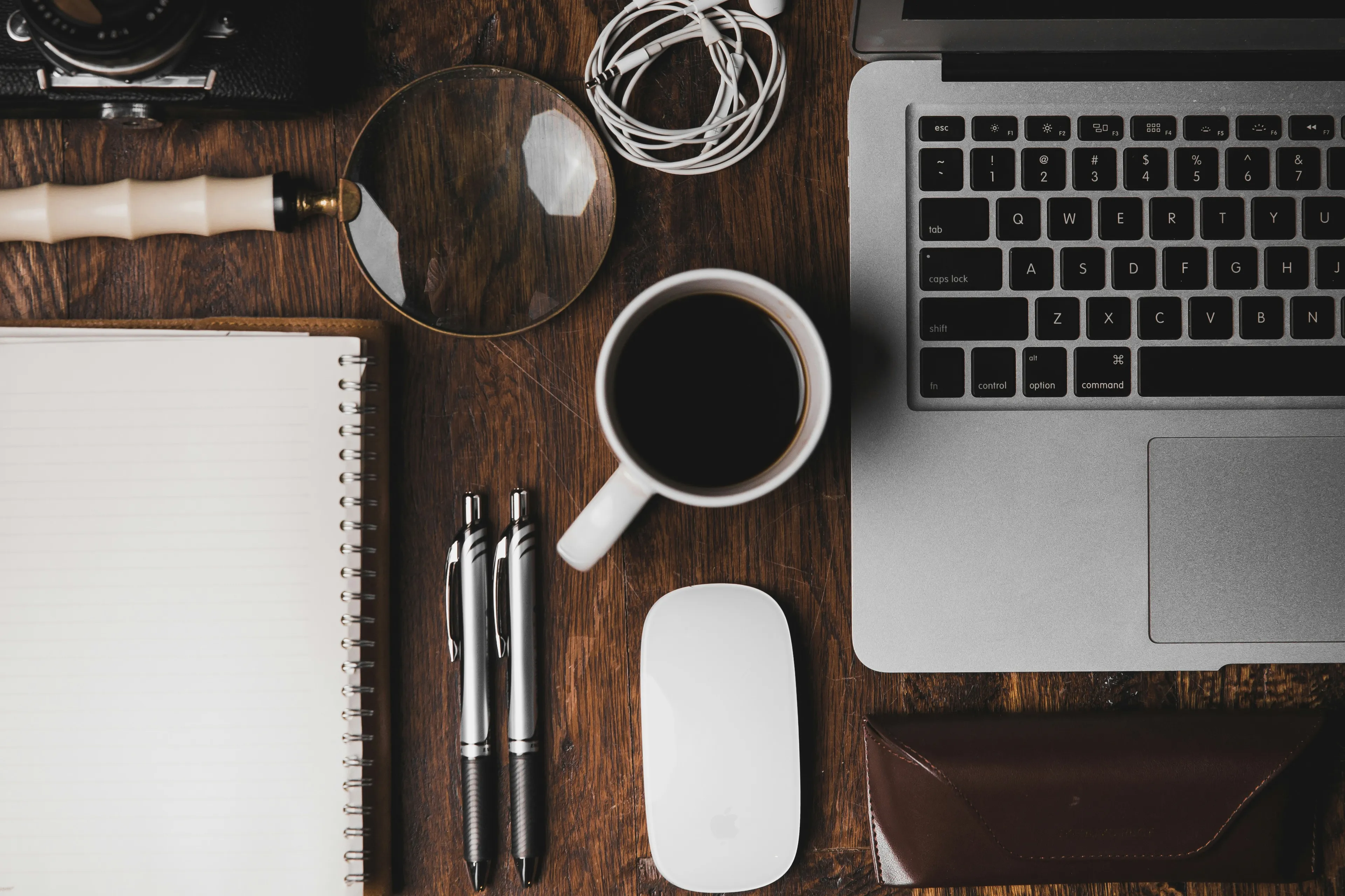 a table with a laptop, a notebook, a pen and a cup of coffee