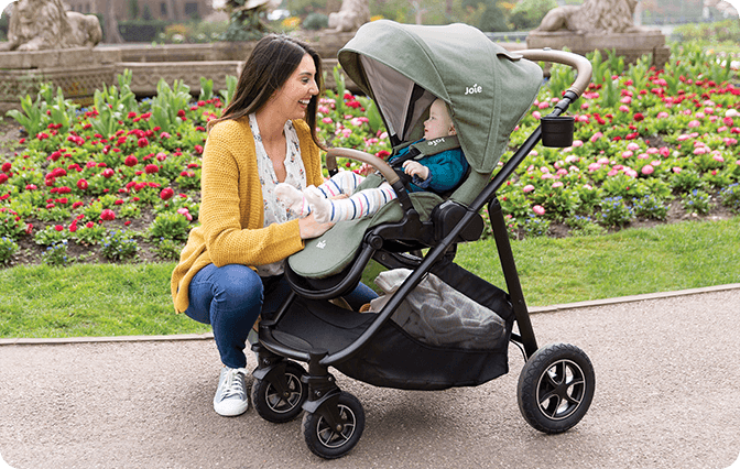 Mom kneeling to interact with young toddler in Joie Signature versatrax pram in light green.