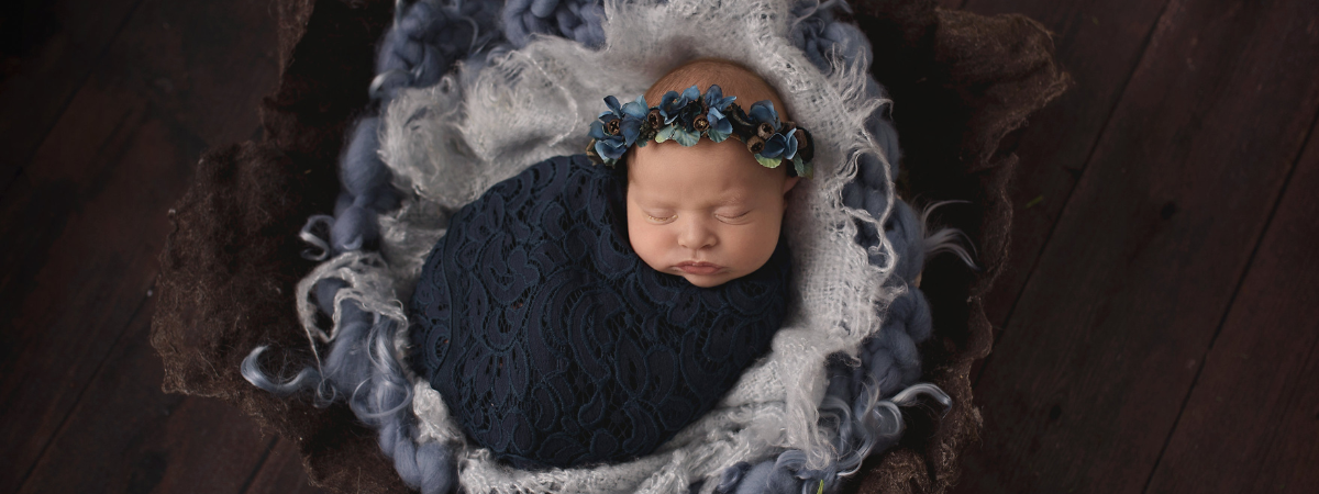 Gabby as a newborn in a black swaddle wearing a halo of flowers