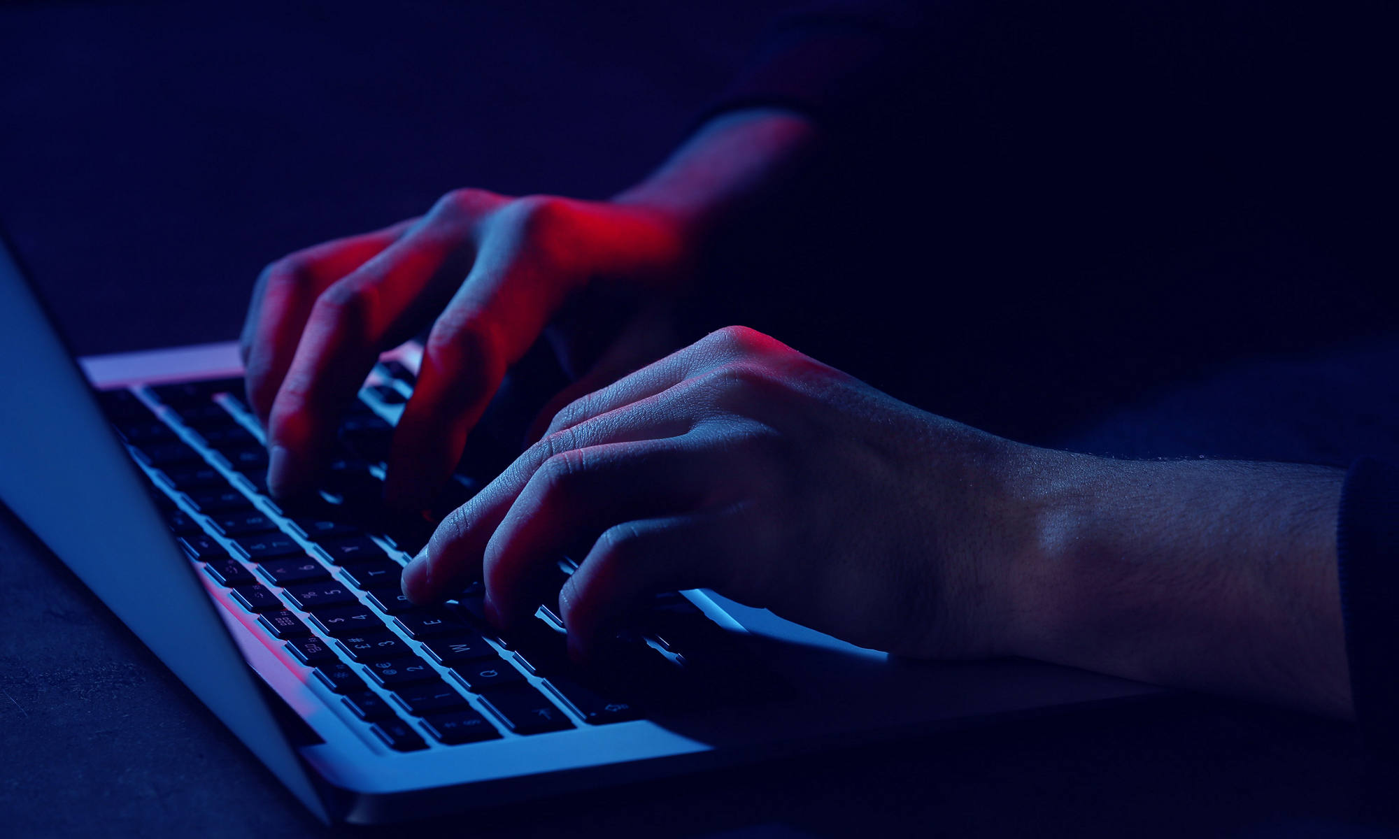 Close up of two hands typing on at a laptop in low light