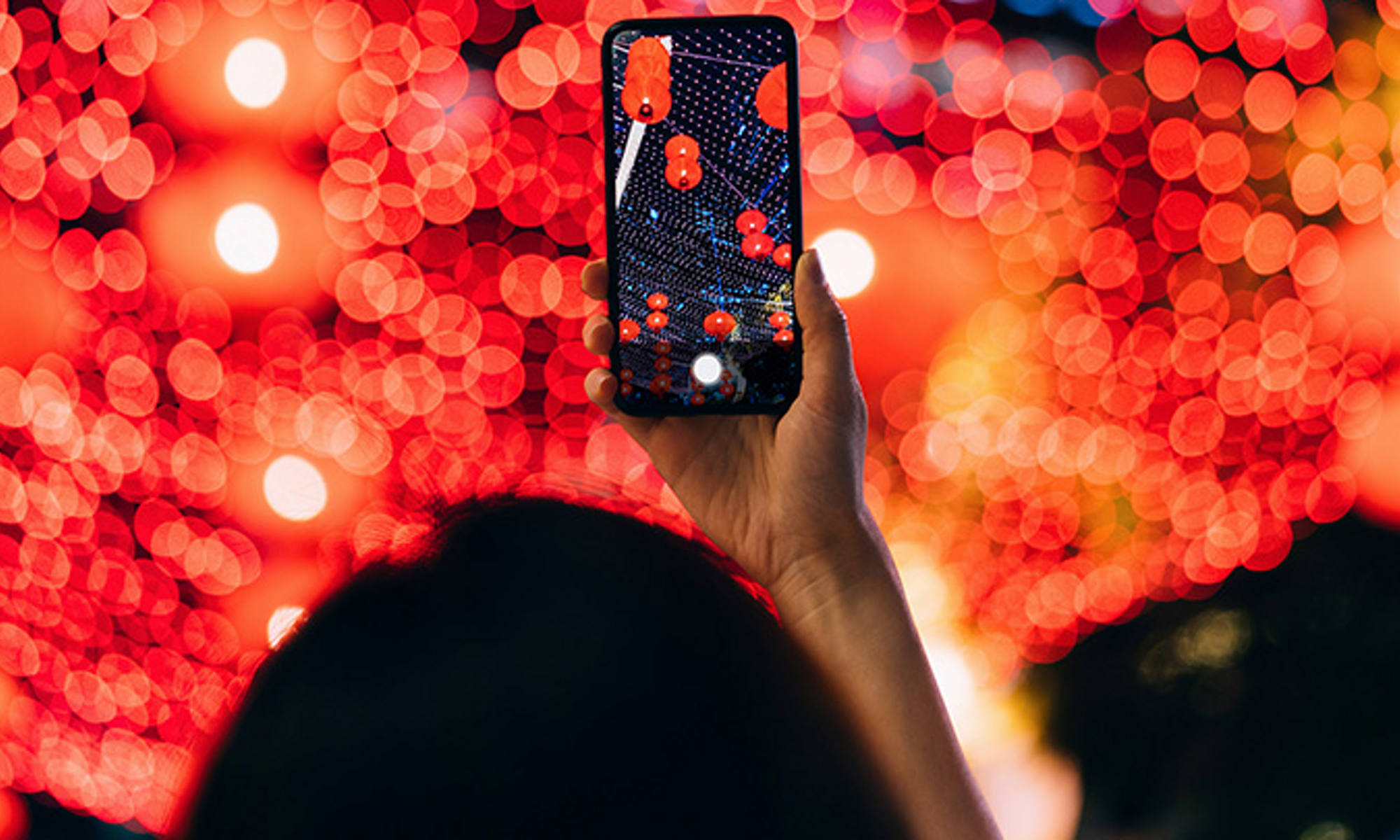 A view from above of someone holding their cell phone out over a sea of blurred bright lights in red and orange hues