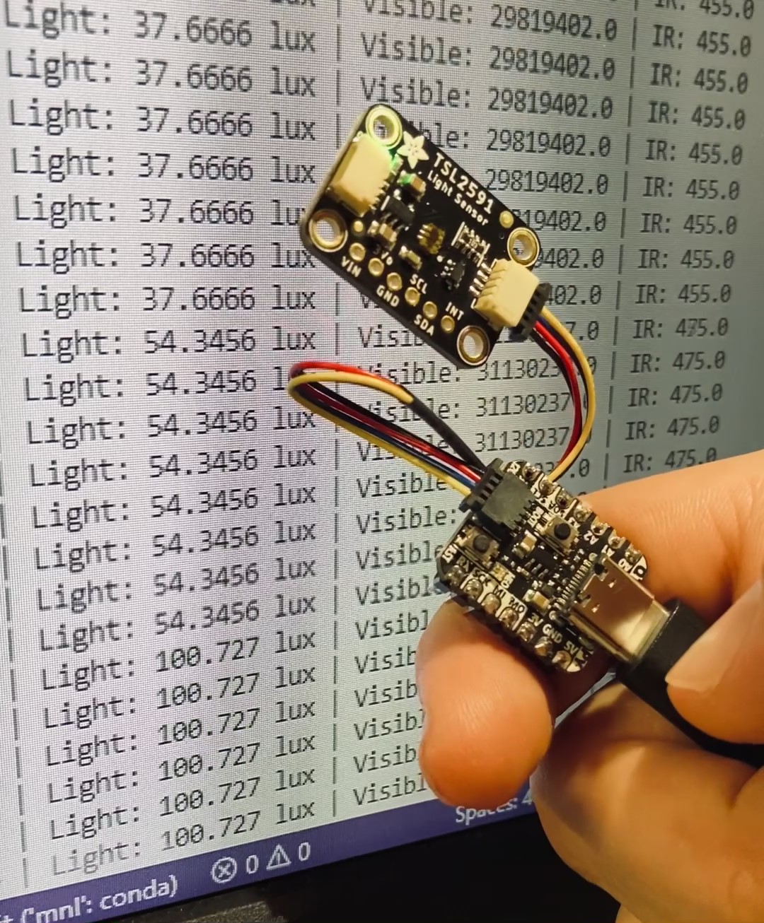 QT Py with light sensor in front of a screen that displays the light values being printed out