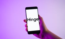 A person is holding a mobile phone with the Hinge logo on its screen