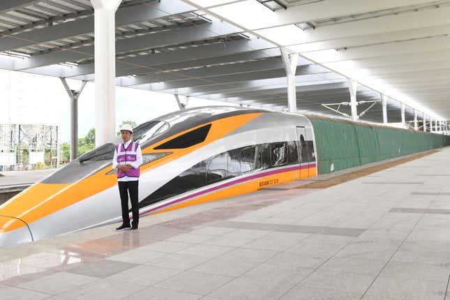 Indonesian president Joko Widodo stands on the platform in a purple vest and white hard hat next to the new high-speed train. 