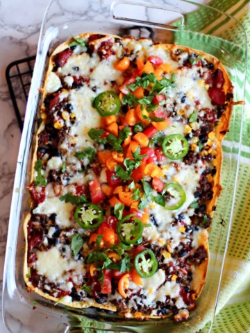 Layered Mexican Casserole in a 9 x 13 pyrex dish with ground beef and corn tortillas, garnished with tomatoes and cilantro