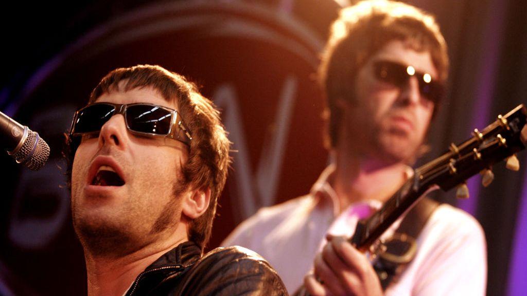 Close up shot Liam Gallagher singing, Noel Gallagher is playing guitar behind him