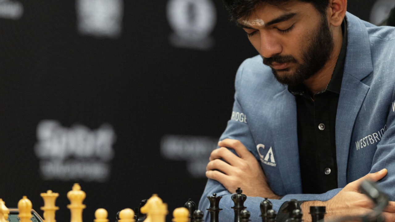 Gukesh Dommaraju gazes down at the chess board at the game on Thursday. He is wearing a blue jacket and a black shirt and has his arms folded, with his elbows resting on the table