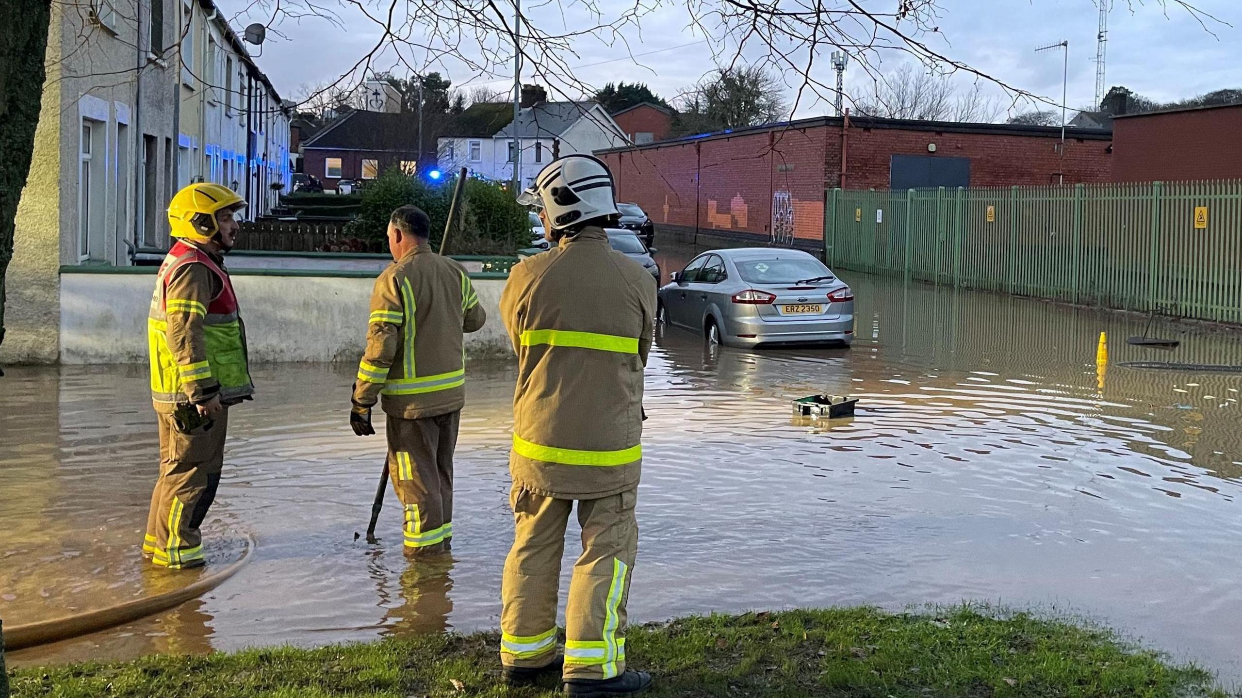 Three firefighters in uniform on residential streets in Belfast conduct a search as a cars tyres are submerged