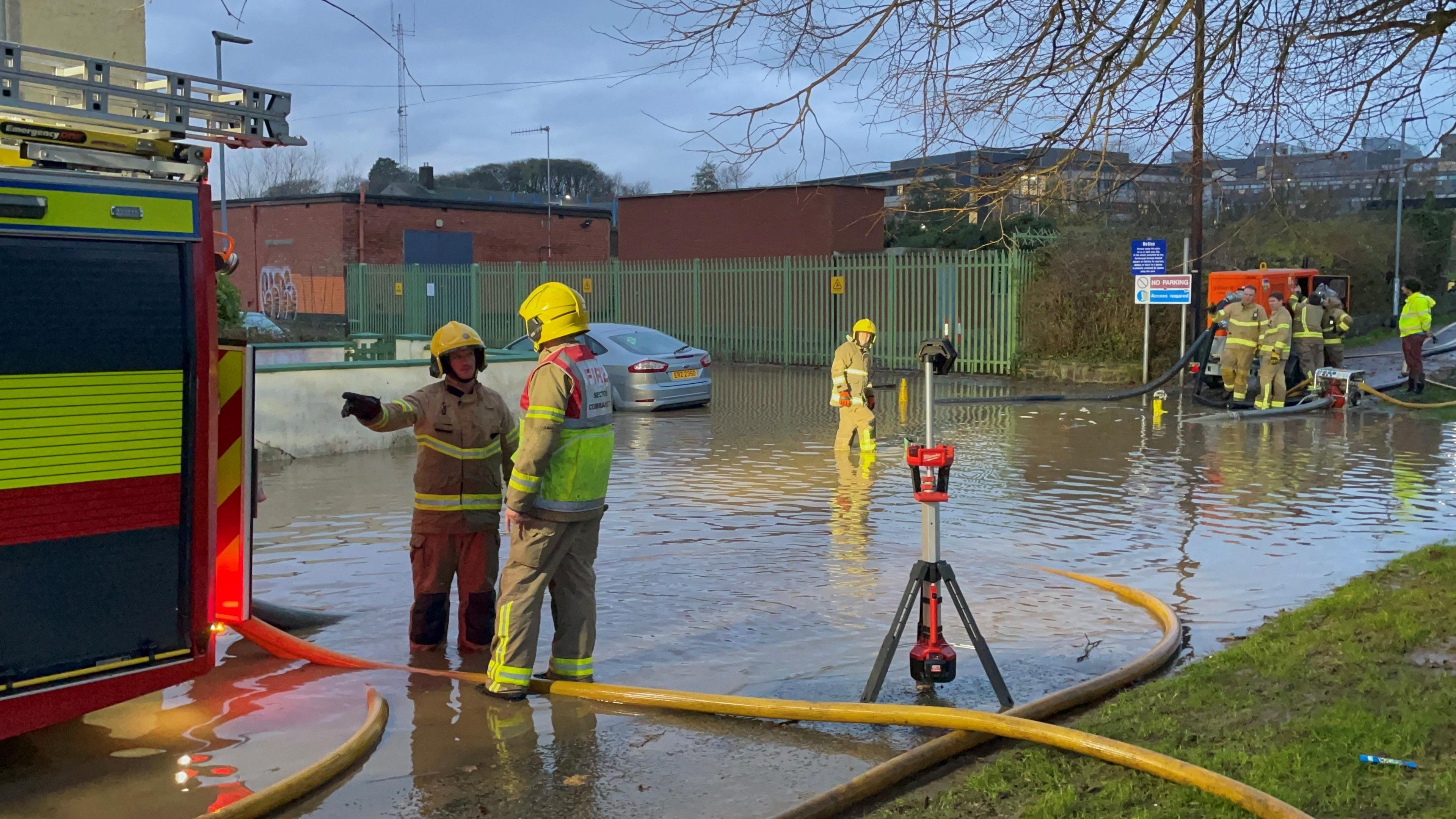 Firefighters in uniform work to pump water away from flooded residential streets near Moat Park in Dundonald on the outskirts of Belfast