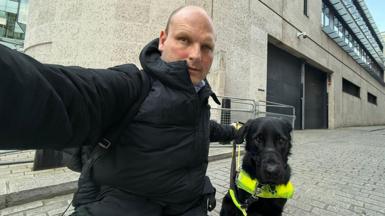 Sean Dilley is wearing a black jacket as he kneels down to take a selfie with his guide dog Shawn