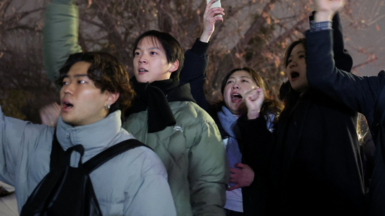 Young people in puffer jackets hold their fists and phones in the air as they shout slogans while protesting outside the National Assembly on Tuesday