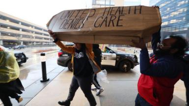 Protestors carry a fake coffin that reads: United Health Denies Care