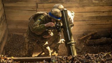 Two Ukrainian soldiers lean over a mortar in a wooden ditch preparing to fire at Russian positions in the Sumy region on 30 September 2024