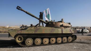 A Syrian rebel fighters waves the flag of Hayat Tahrir al-Sham (HTS) on top of a tank in Saraqeb, Idlib province, Syria (1 December 2024)