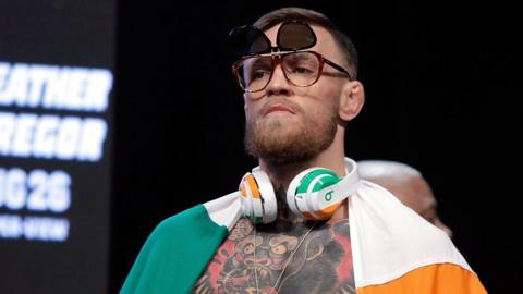 Conor McGregor wearing sunglasses, headphones, and an Irish flag