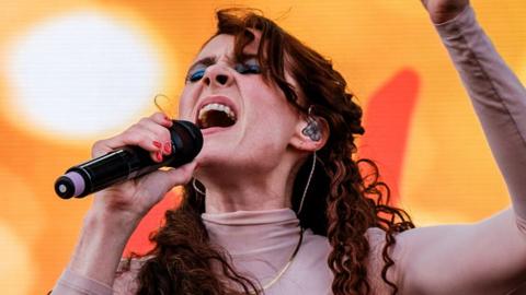 Kate Nash singing on stage against an orange backdrop