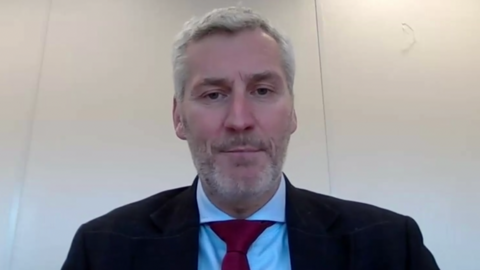 Pete Bond looks at the camera. He has short, grey hair and red tie, blue shirt and dark suit jacket.