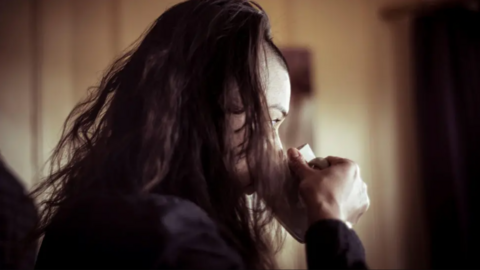 A woman looking away from the camera in partial shadow, drinking from a coffee mug