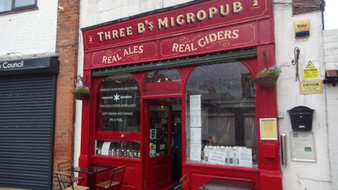 Red-fronted exterior of The Three B's micropub with chairs and tables outside.