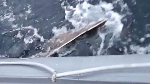 Phone footage of a skate surfacing out of grey waves to a rigid inflatable boat.ttack the side of a inflatable