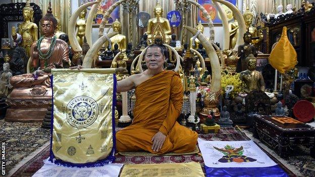 Thai Buddhist monk Phra Prommangkalachan holding a banner emblazoned with sacred patterns surrounding Leicester City Football Club's crest as he poses for pictures at the Traimitr Withayaram Woraviharn Temple in Bangkok