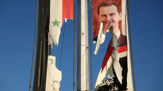 A billboard bearing a picture of Syria's President Bashar al-Assad and a national flag are torn by anti-government fighters in the northern city of Aleppo