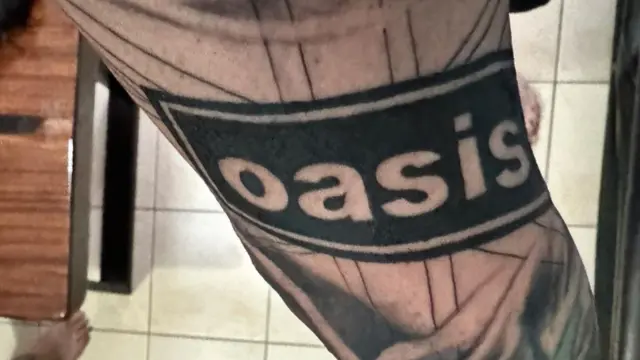 Oasis tattoo with black background and white/see through writing saying 'oasis' on person's forearm