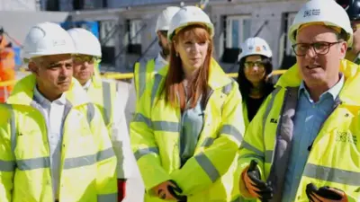 Sadiq Khan, Angela Rayner and Sir Keir Starmer wearing hi-vis jackets and white hard hats on a building site