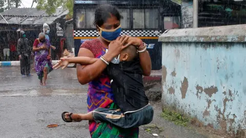 Reuters A woman carries her son as she tries to protect him from heavy rain while they rush to a safer place, following their evacuation from a slum area before Cyclone Amphan makes its landfall, in Kolkata