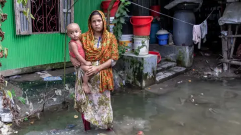 Women holds child whilst standing in flood waters in Bangladesh