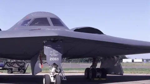 A B2 Stealth Bomber 393 BS US Airforce - a dark grey airplane with flag wings and a rounded top - sits on the tarmac at IAT Air tattoo RAF Fairford