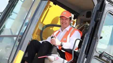 Jeremy Fish Jeremy Fish wearing an orange hi-vis vest and cap while sitting in a yellow digger