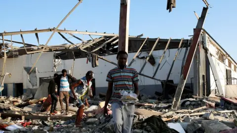 Reuters Migrants carry the remains of their belongings from among rubble at a detention centre for mainly African migrants that was hit by an airstrike in the Tajoura suburb of the Libyan capital of Tripoli, Libya July 3