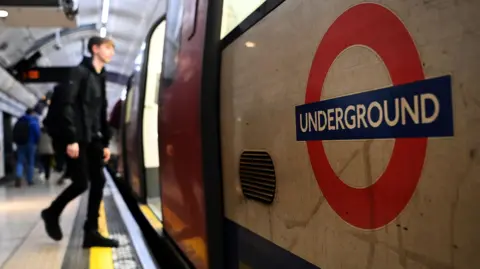 File image showing a man dressed in black boarding a London Underground Tube carriage, with a close-up of the underground roundel logo on the carriage