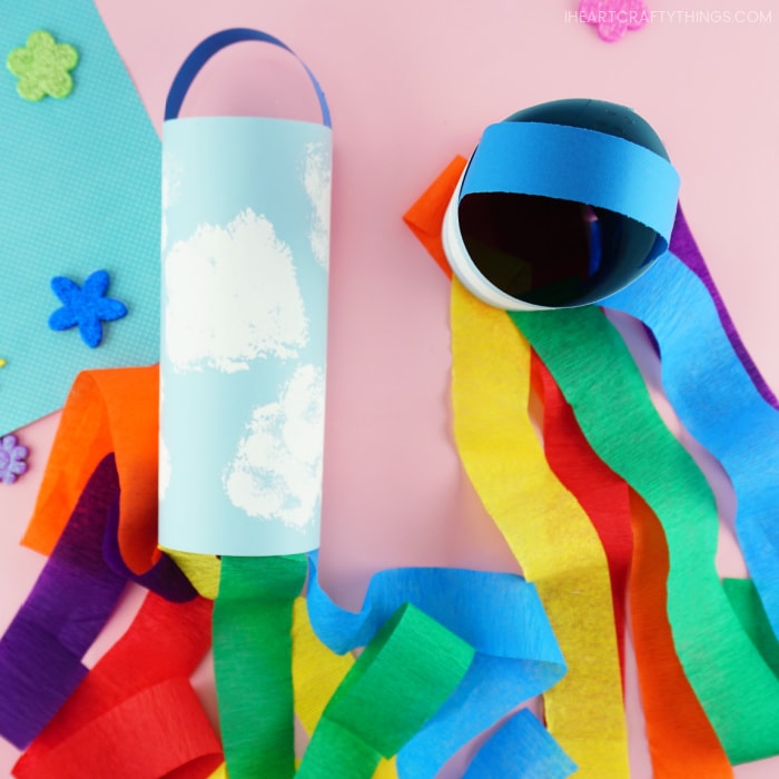 Two rainbow windsocks with one laying flat showing the front view of it and one standing up showing the top view of the windsock.