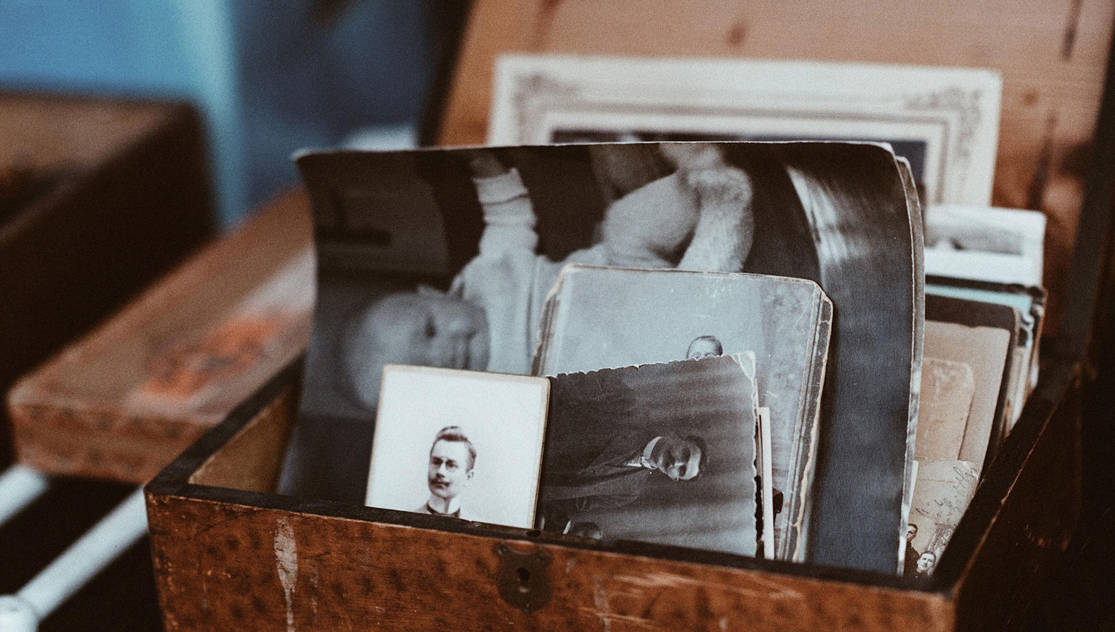 A wooden box filled with vintage black-and-white photographs, showing portraits and various scenes, some faded with age.