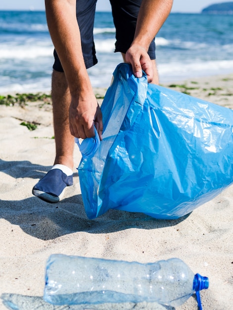 Foto grátis homem coletando lixo plástico da praia e colocá-lo em sacos de lixo azuis para reciclagem