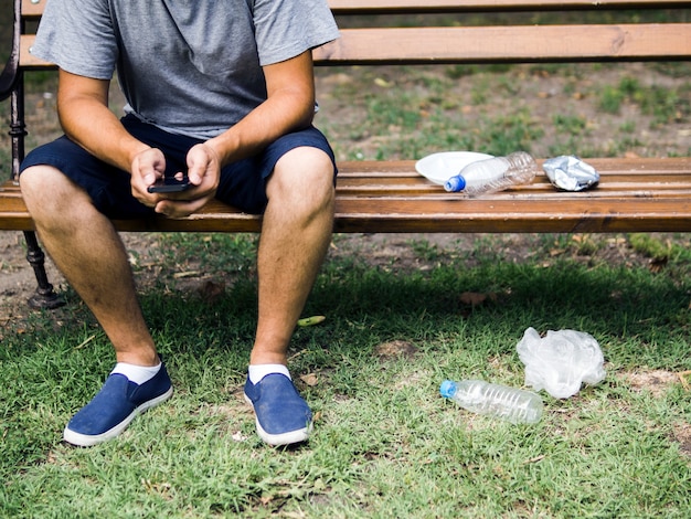 Foto grátis homem, usando, cellphone, sentando, ligado, banco, perto, lixo plástico, parque