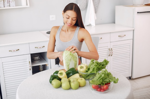 Foto grátis mulher bonita e desportiva em uma cozinha com legumes