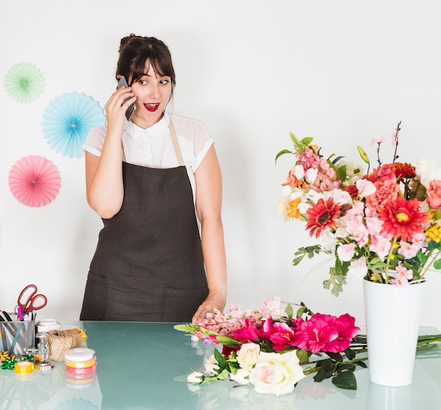 Foto grátis mulher surpreendida falando no smartphone com ramo de flores na mesa