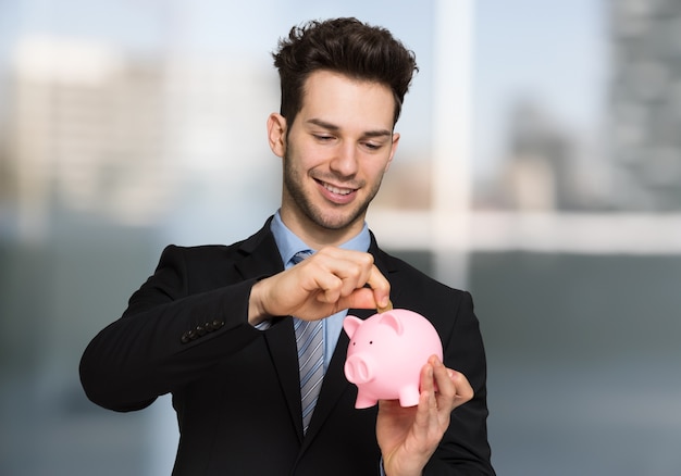 Jovem empresário bonitão colocando dinheiro em um cofrinho